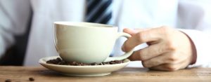 A cup of coffee and a hand on the mug. Coffee is common in recovery and the person with the coffee is a businessman seeking help.